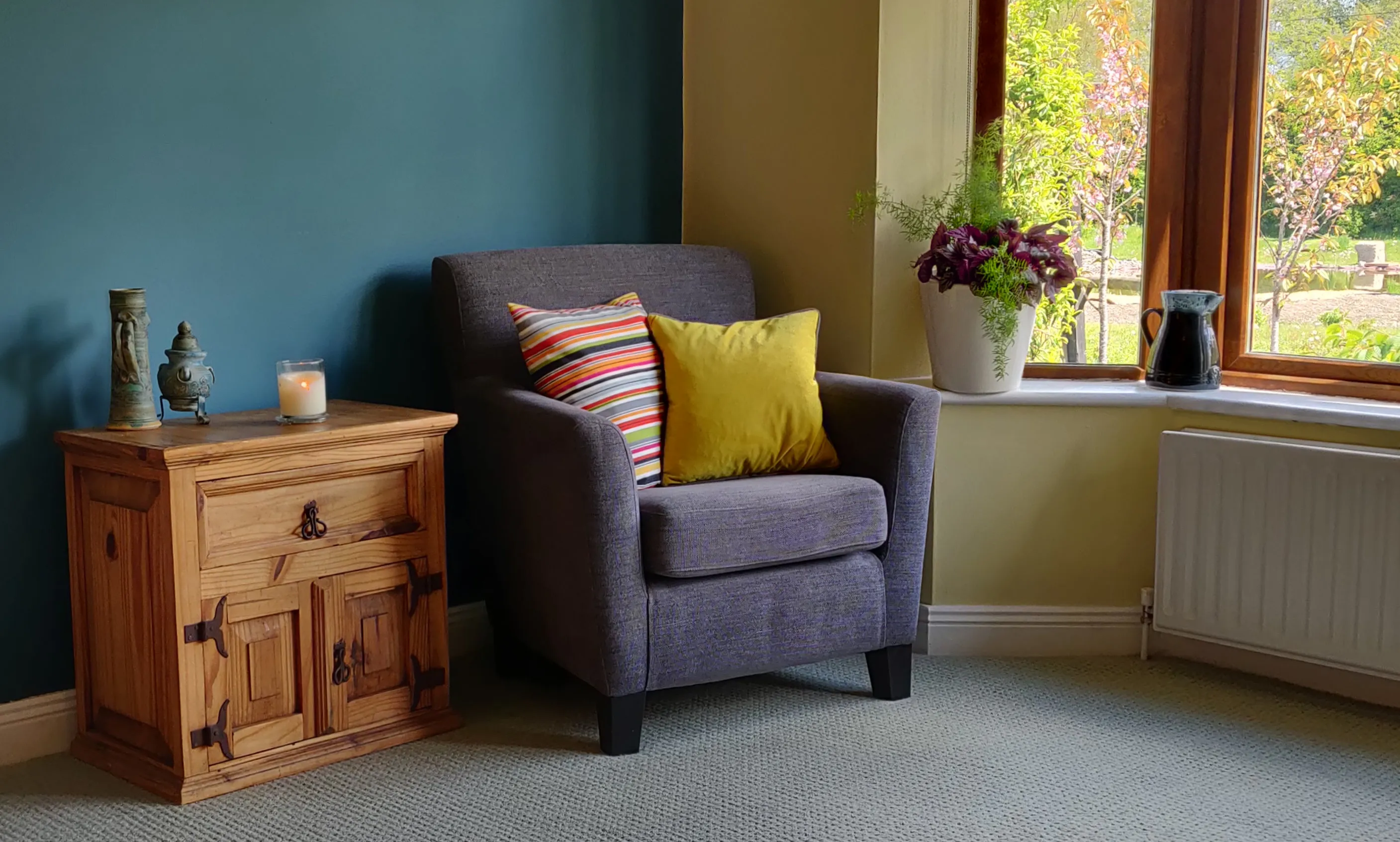 The therapy room, an inviting armchair with cushions in a warm room with a view of a garden outside