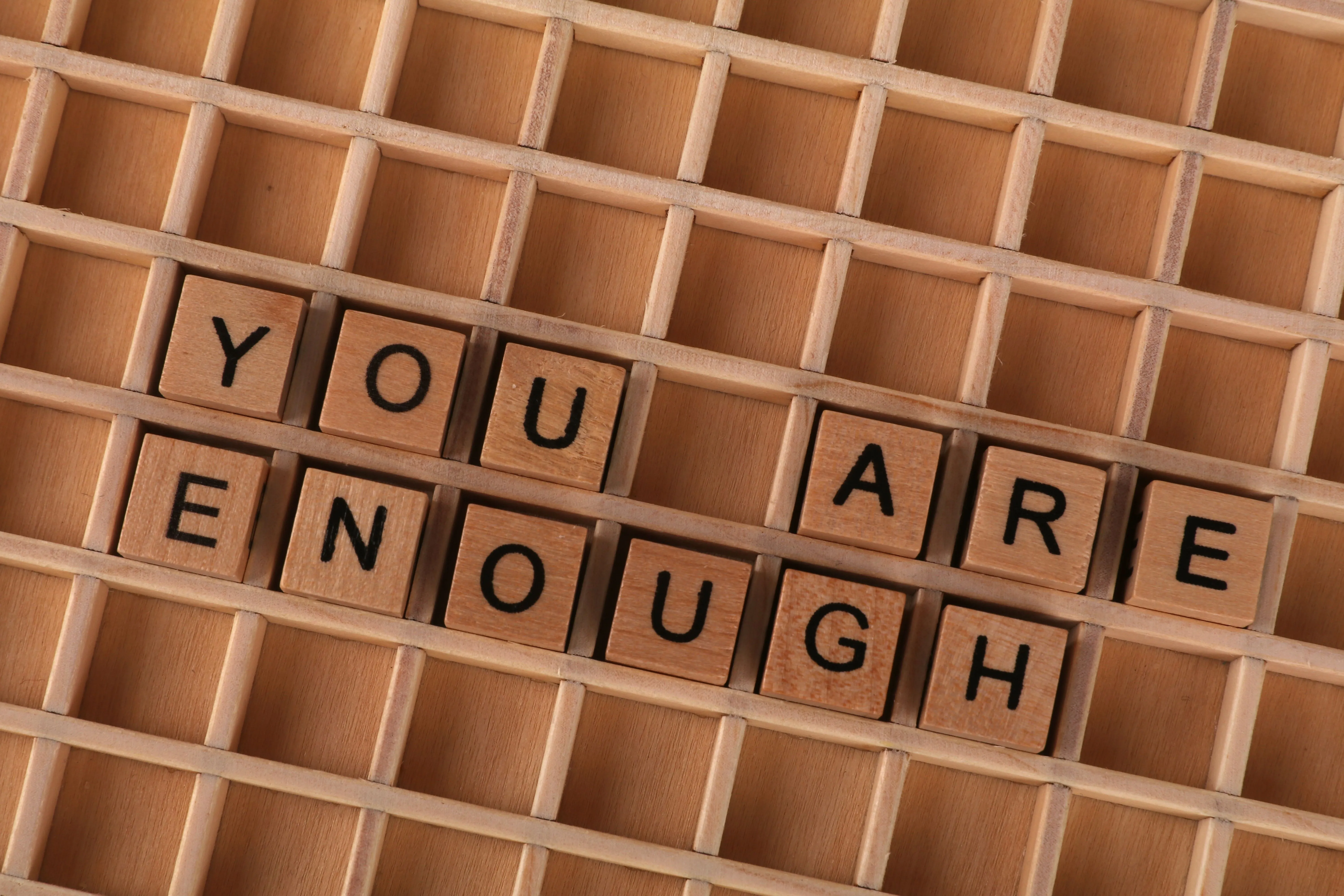 Wooden letter tiles spelling "you are enough" in a wooden letter tray