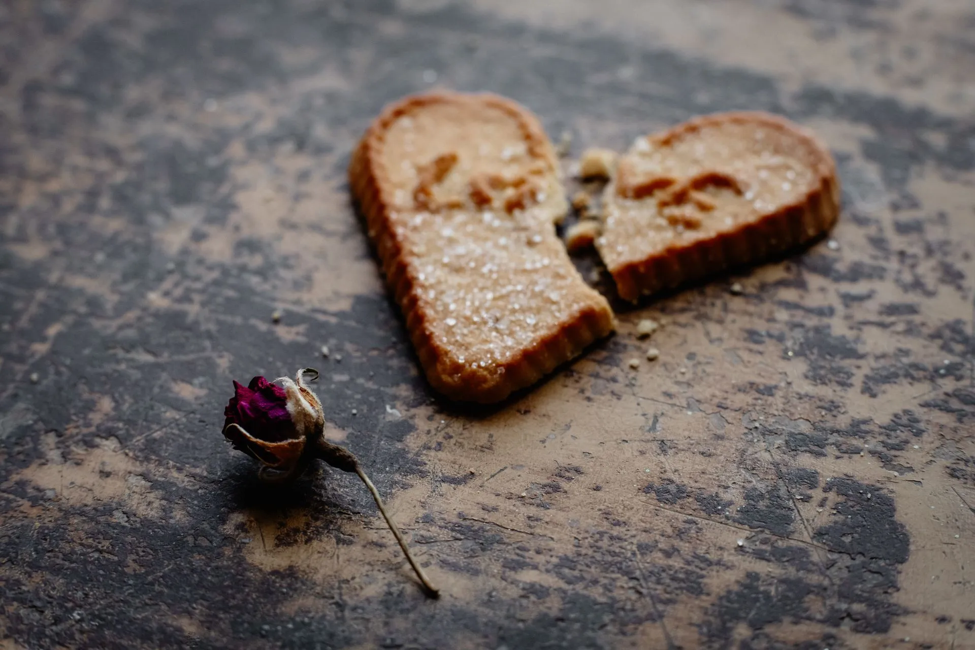 Broken heart-shaped biscuit with a dried rose bud on a rustic surface